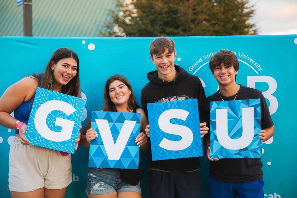 students posing in front of  backdrop at Laker Kickoff photo booth holding GVSU letters
